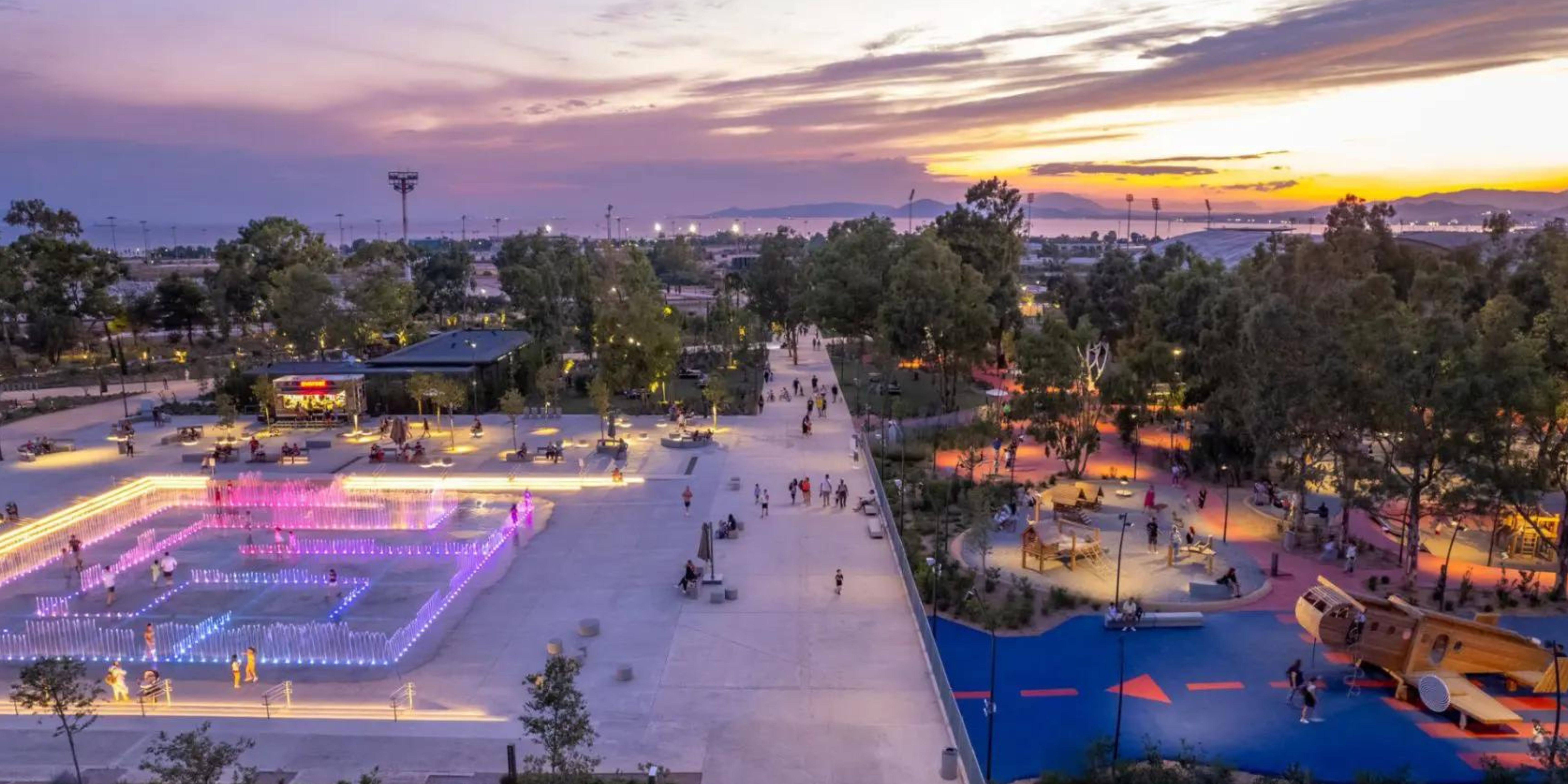 Evening view of Ellinikon Experience Park with lit fountains and recreational areas.